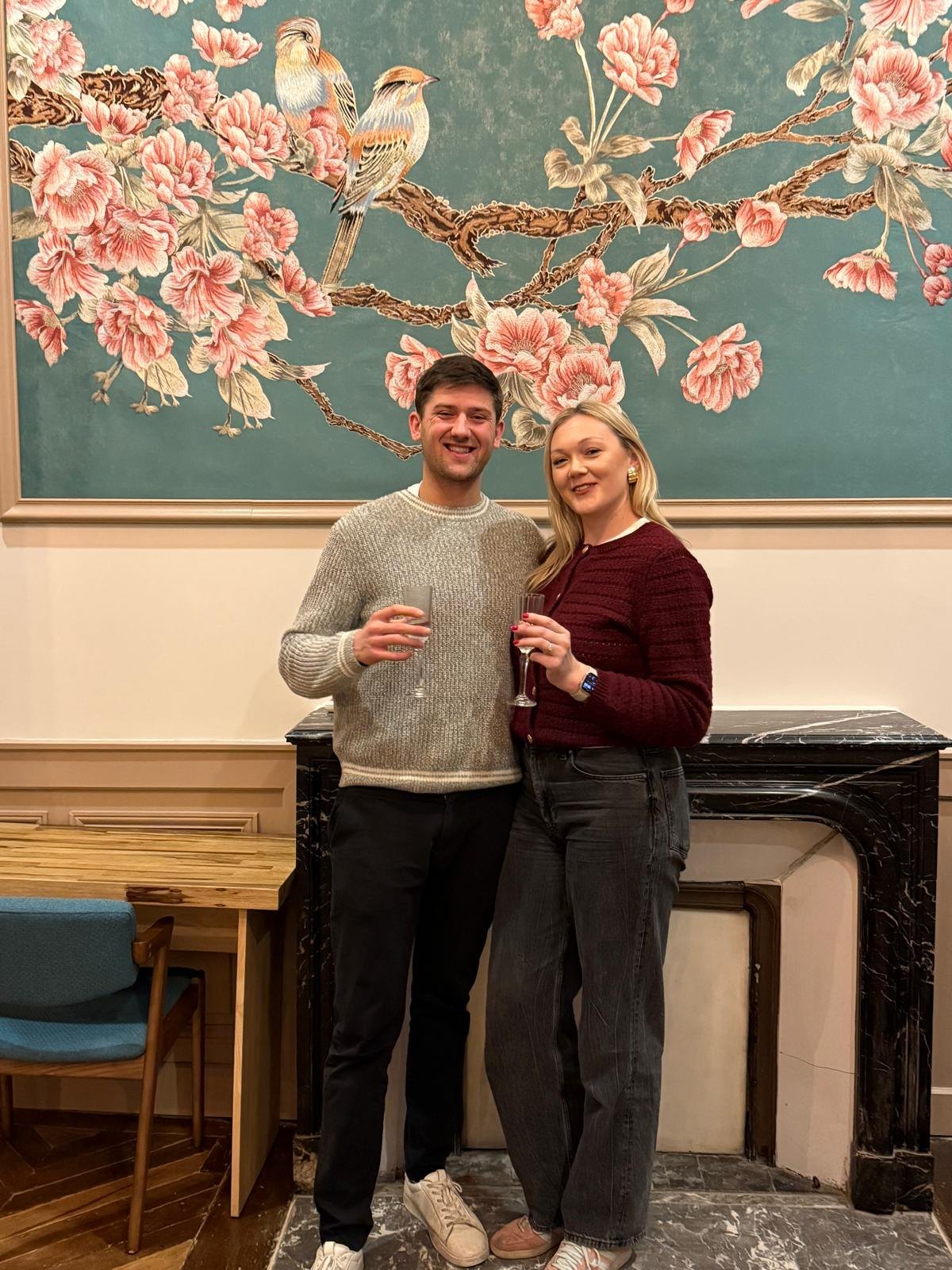 George and Alex with drinks beside a floral mural